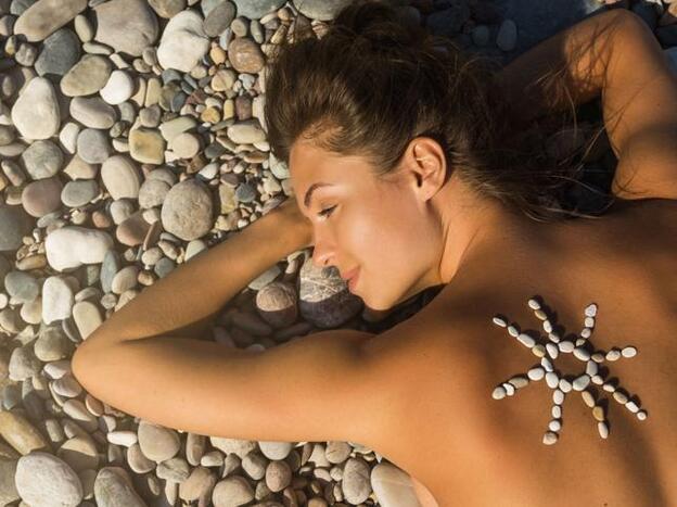 Mujer tumbada en una playa de piedras./Fotolia