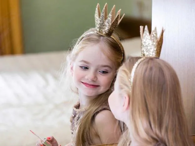 Una niña con corona mirándose en el espejo./adobe stock