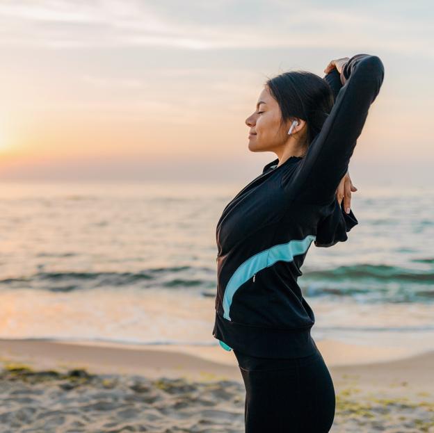 Mujer estirando después de hacer ejercicio en la playa al amanecer. 