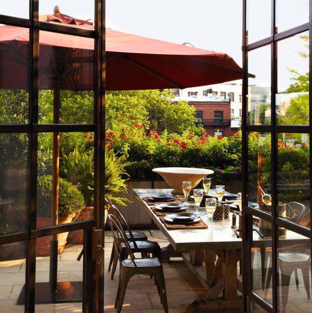 Panorámica de la amplia terraza del apartamento, donde se ha colocado una mesa de comedor y una sombrilla de color terracota.